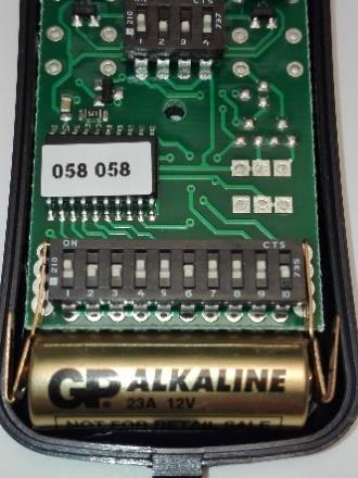 Carte électronique ouverte montrant les deux rangées de dip switchs et la pile 23A 12V
